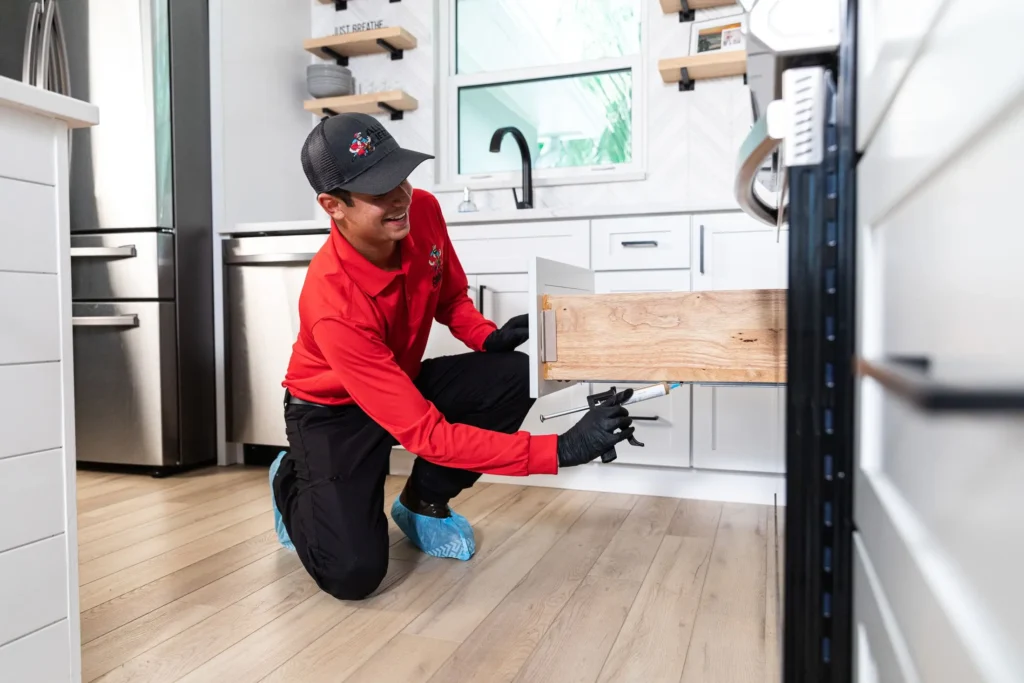 worker applying pest solution to kitchen cabinet