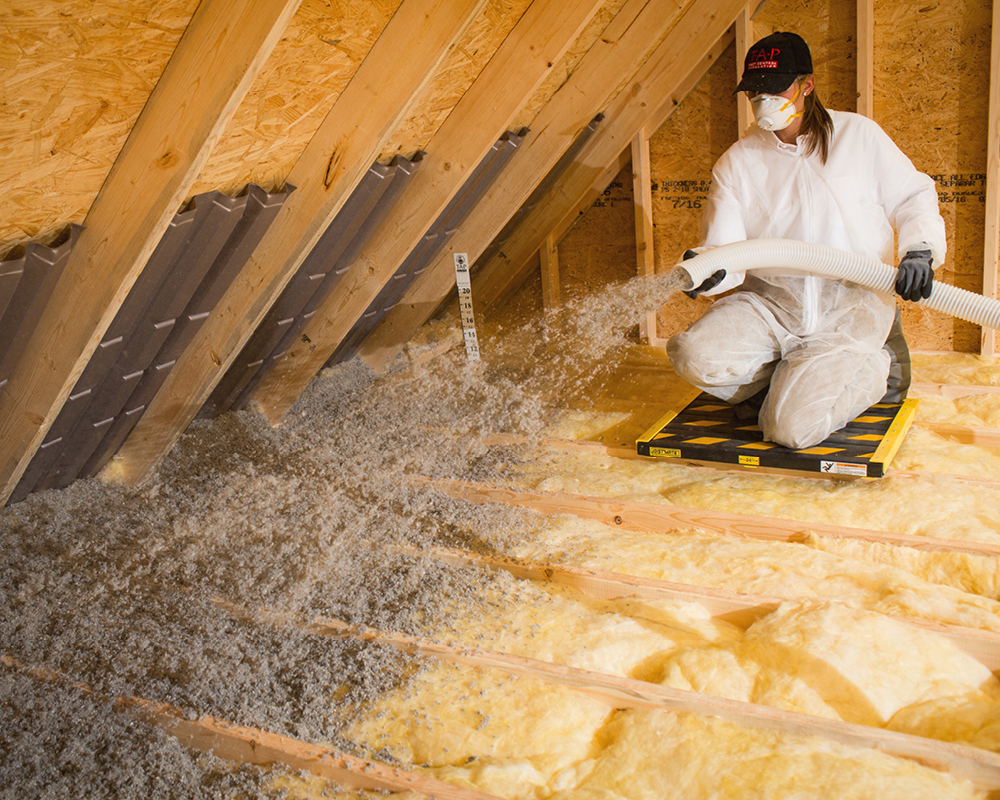 A technician blowing in pest control insulation into the attic covering the old fiberglass insulation