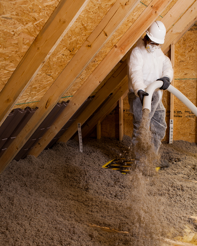 A technician standing blowing TAP insulation into the attic while wearing protective gear